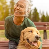 A senior woman smiles as she holds her golden retriever dog in the park