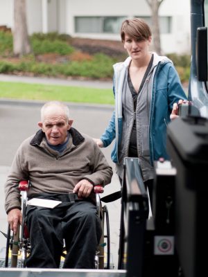 A senior man is being helped into a wheelchair accessible van